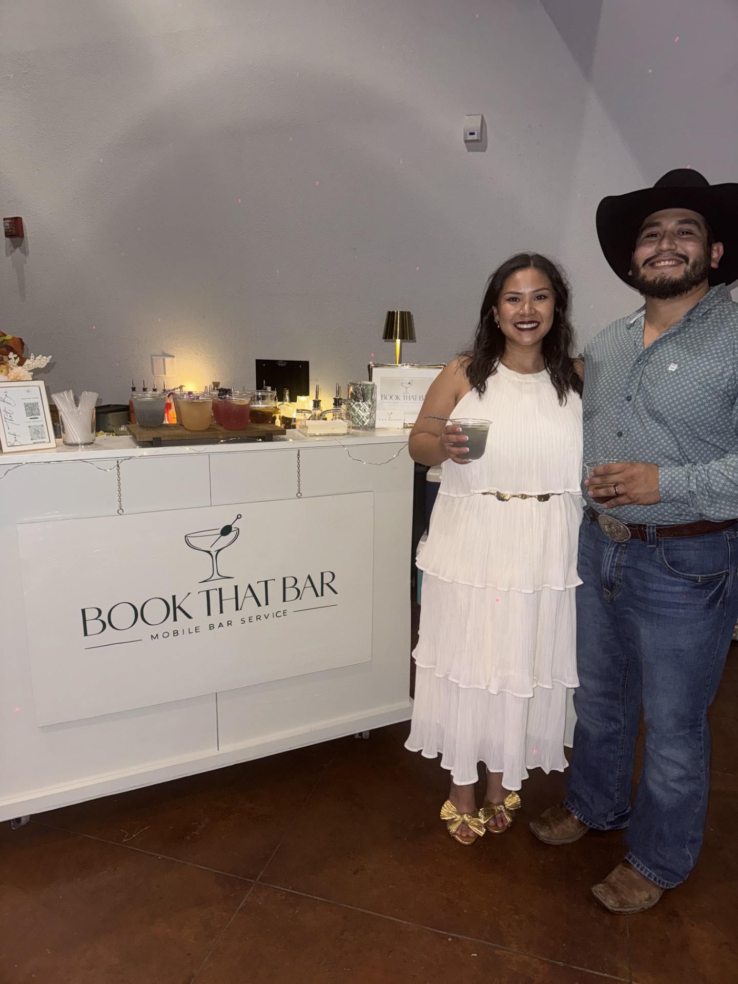 A smiling couple holding drinks beside the Book That Bar setup