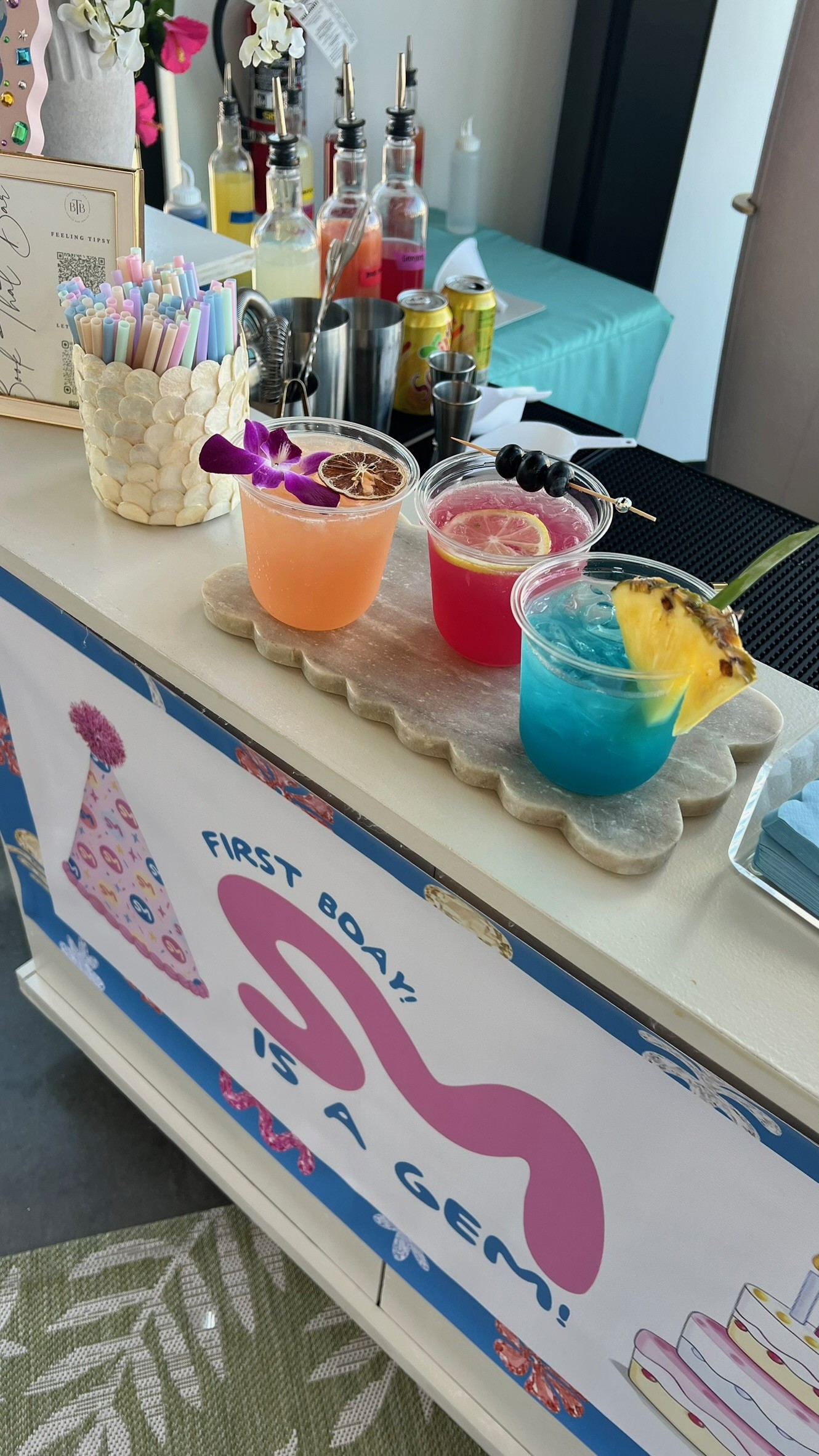 Three colorful garnished drinks on a customized birthday bar