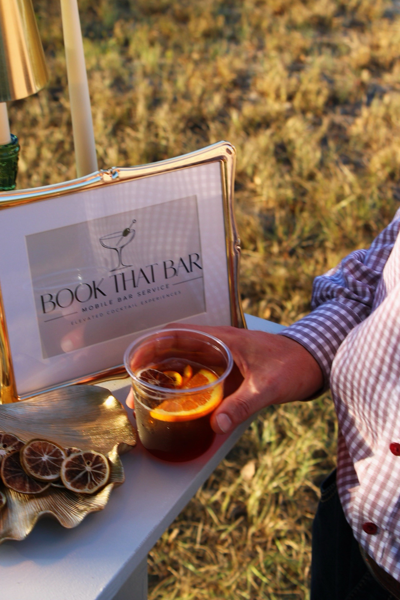 A guest holding a whiskey cocktail beside the Book That Bar sign